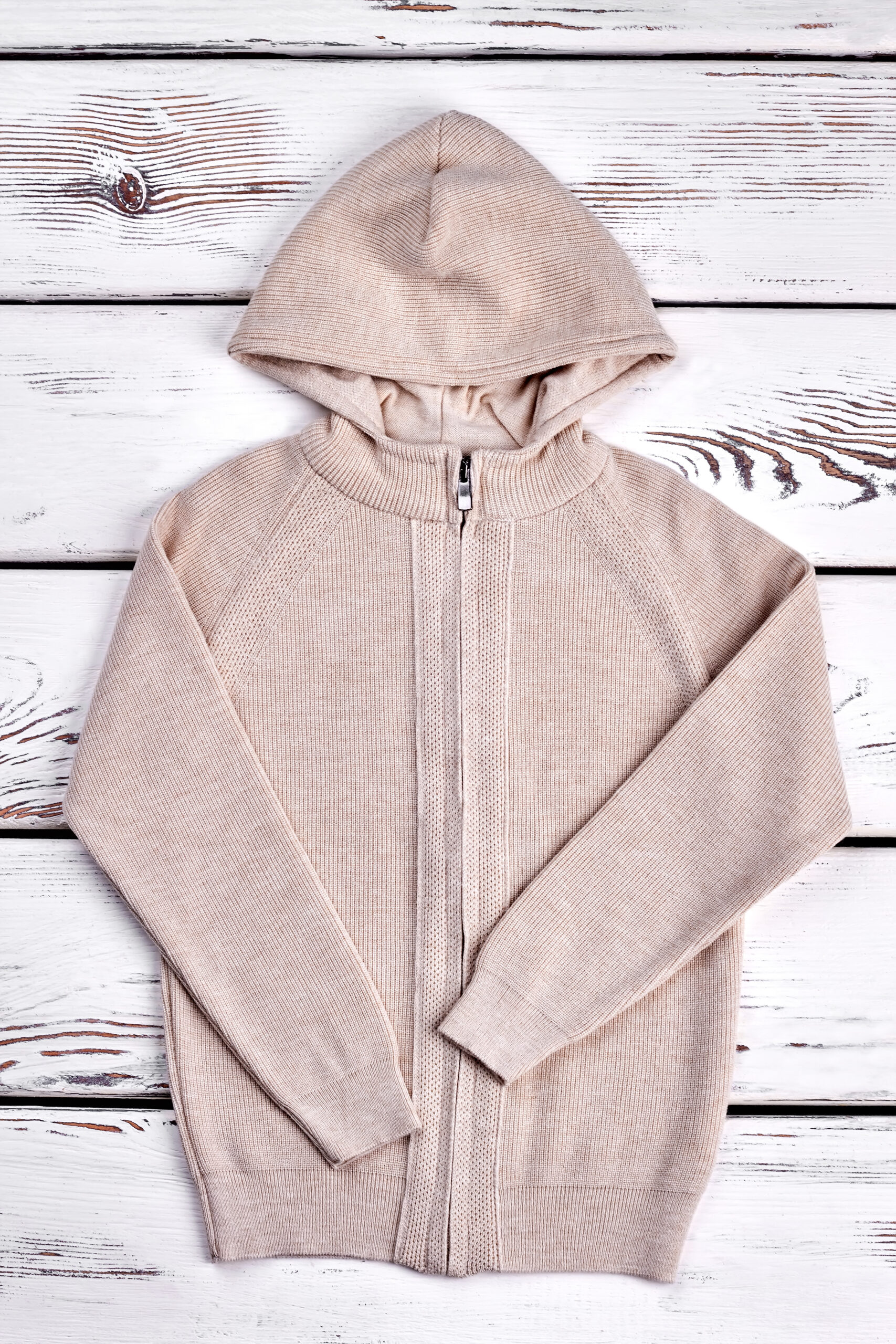 Top view of knitted pullover for kids. Children casual warm zipper sweater on vintage wooden bckground. Beautiful beige color warm cardigan for kids.